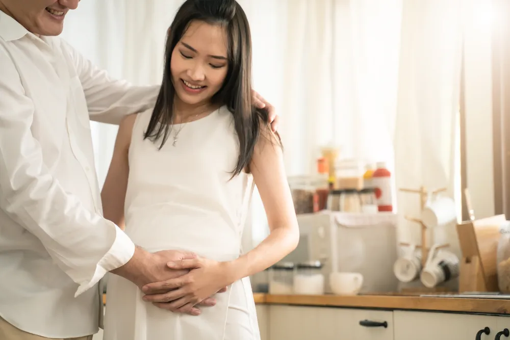 Smiling couple holding a positive pregnancy test while celebrating an early pregnancy after their fertility journey.