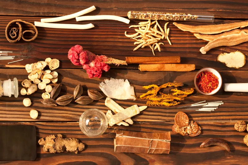 Assortment of traditional Chinese medicinal herbs and acupuncture needles arranged on a wooden table, illustrating herbal medicine used in Traditional Chinese Medicine (TCM).