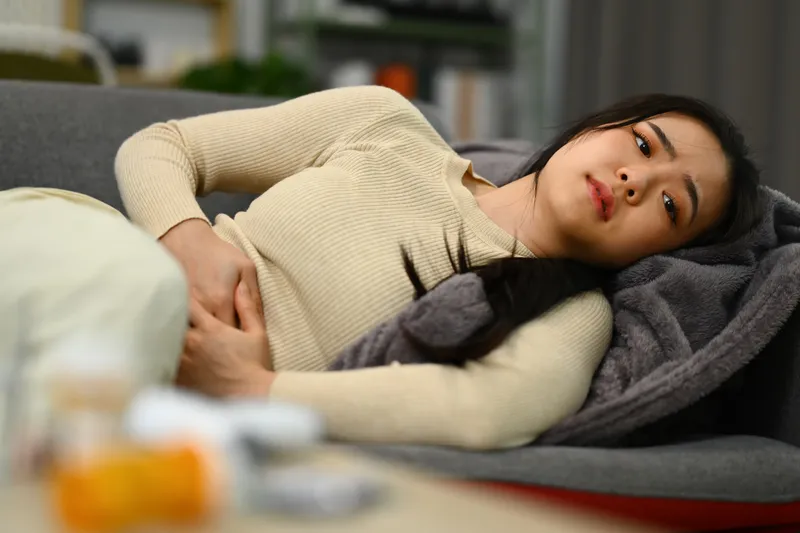Woman lying on a sofa while holding her lower abdomen, depicting menstrual pain or discomfort associated with irregular menstrual cycles.