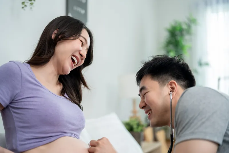 Expectant father listening to a pregnant woman's baby bump while the couple shares a joyful moment