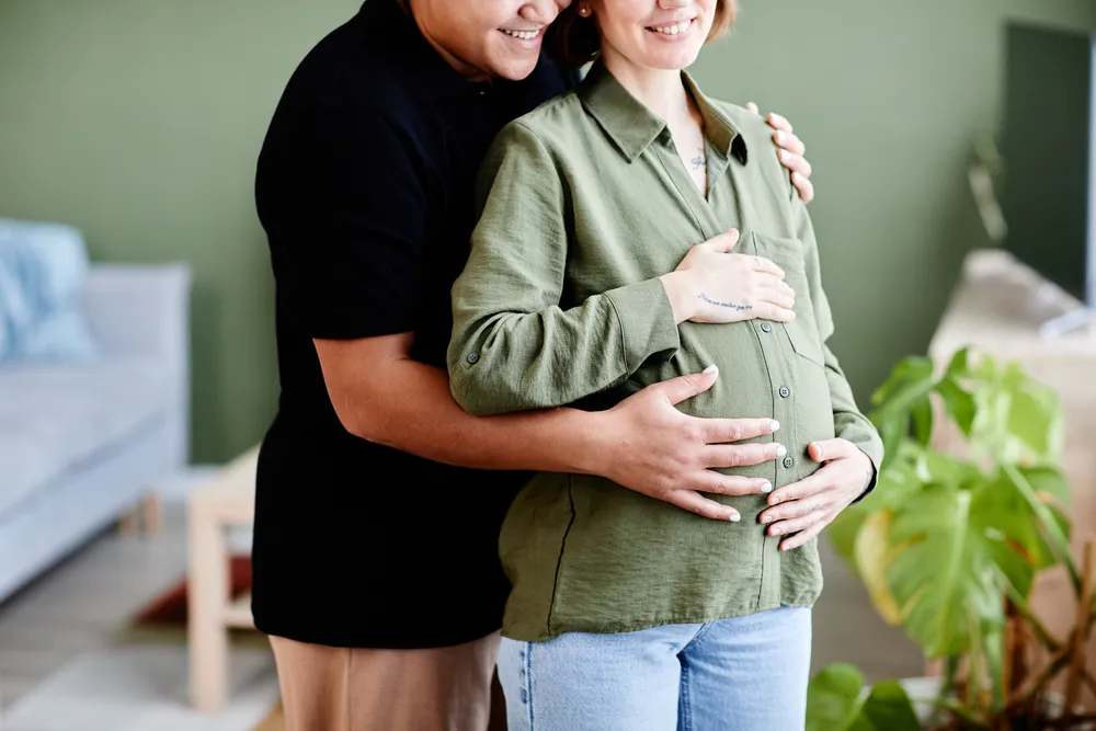 Expectant couple embracing while gently holding a pregnant baby bump at home