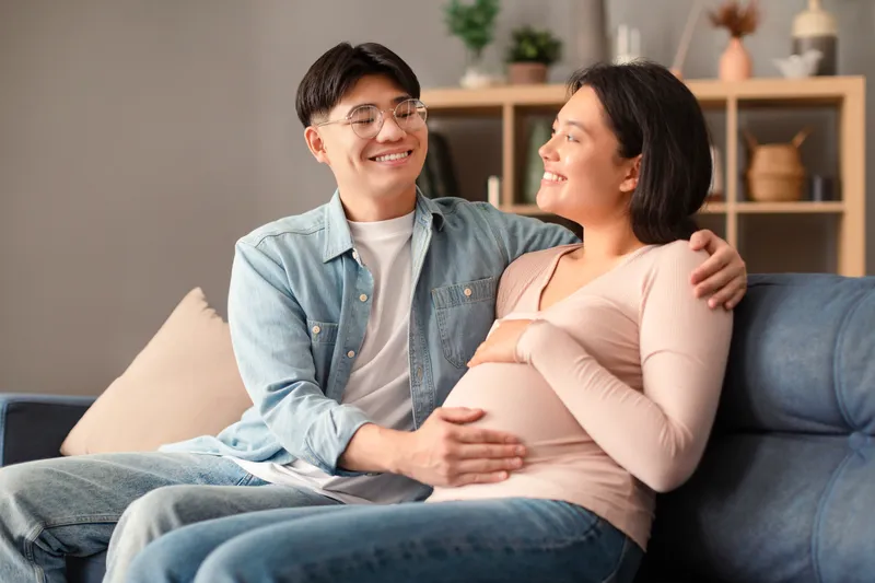 Expectant couple smiling while gently holding a pregnant baby bump at home