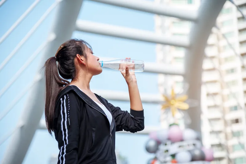 Woman drinking water outdoors after exercise to stay hydrated in Singapore's warm and humid climate.